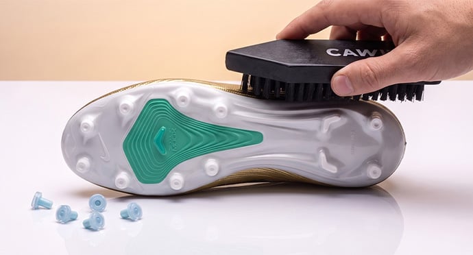Brushing the SG sole of a football boot with removed screw-in studs lying in front