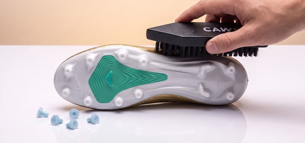 Brushing the SG sole of a football boot with removed screw-in studs lying in front