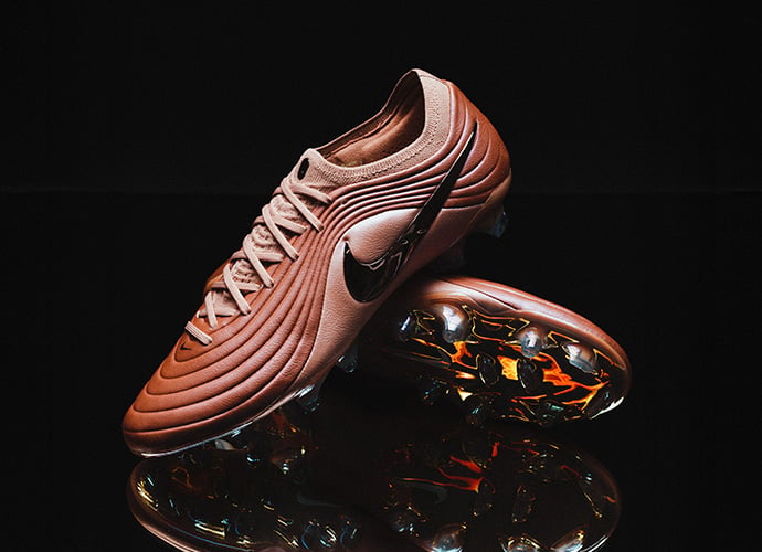 Nike Tiempo Maestro football boots in rose gold/copper finish showcasing wavy ribbed upper design and reflective soleplate with colorful metallic studs against black background with reflection