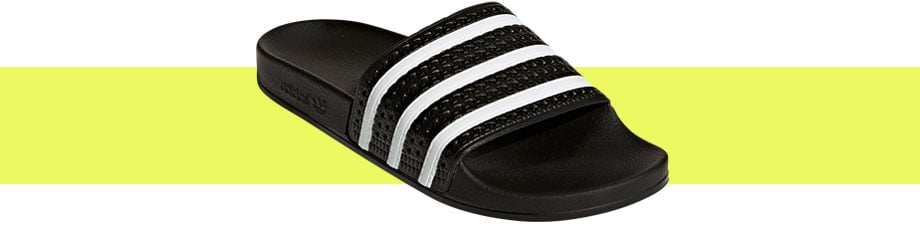adidas Originals Adilette Schwarz Weiß, diagonaler Blick von vorne auf die Badelatsche mit direkter Sicht auf den texturierten Riemen mit den klassischen drei adidas-Streifen