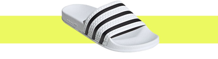 adidas Originals Adilette Weiß, diagonaler Blick von vorne auf die Badelatsche mit direkter Sicht auf den texturierten Riemen mit den klassischen drei adidas-Streifen