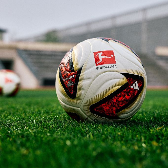 adidas Torfabrik Bundesliga official match ball on green turf with blurred stadium background - white leather surface with red and gold accents