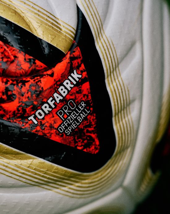 Close-up of adidas Torfabrik Pro football showing red and black branding with 'Official Spielball' text and gold adidas stripes on white panels