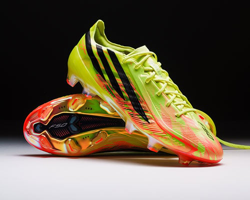 Pair of the adidas F50 Hyperfast Elite FG first launch edition boots arranged: one sideways showing the sole plate. Other boot on top showing lateral outside profile with F50 style streamlined adidas 3-stripes