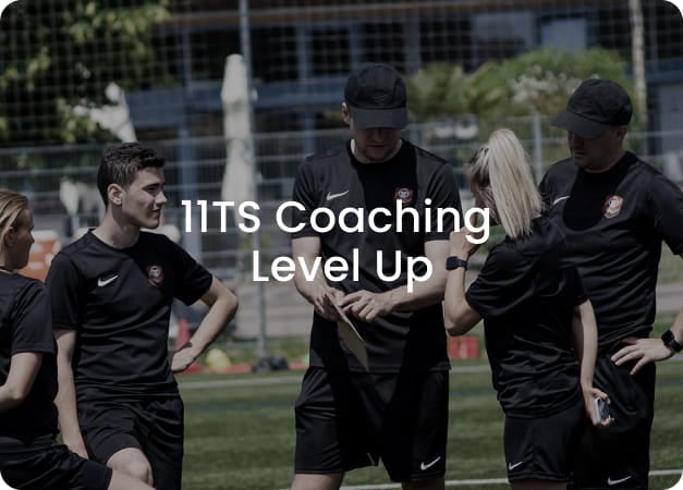 Group of football coaches in black Nike kits discussing tactics on pitch - 11TS Coaching Level Up programme at 11teamsports Academy Variante 2 - Brand & Education-optimized (British):