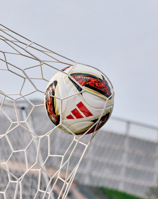 adidas Torfabrik football in goal net showing red and gold design with Torfabrik branding - official Bundesliga match ball caught in white netting