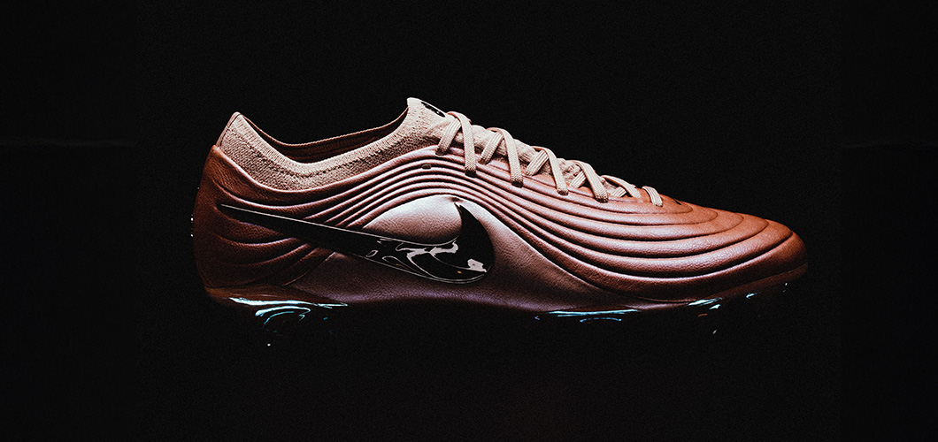 Nike Tiempo Maestro football boot in copper/bronze colorway featuring dynamic ribbed upper design and modern aesthetic against black background