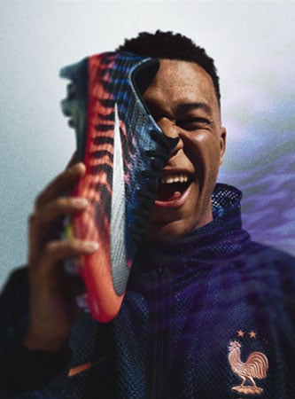 Mbappé in France training gear holding a Nike Mercurial Superfly 11 FG cleat in front of his face covering the right eye