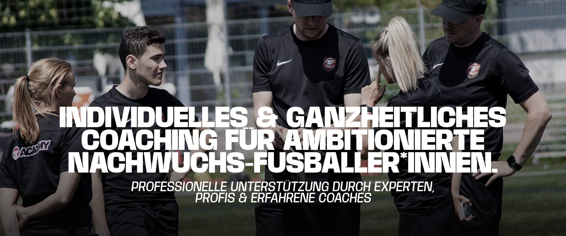 Experienced coaches in black Academy kit discussing tactics with young footballers on pitch - Individual and holistic coaching at 11teamsports Football Academy