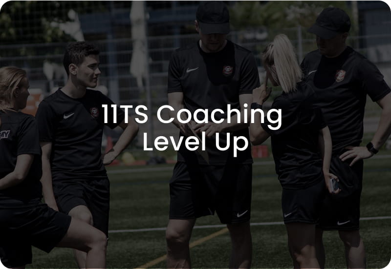 Group of football coaches in black Nike kits discussing tactics on pitch - 11TS Coaching Level Up programme at 11teamsports Academy Variante 2 - Brand & Education-optimized (British):