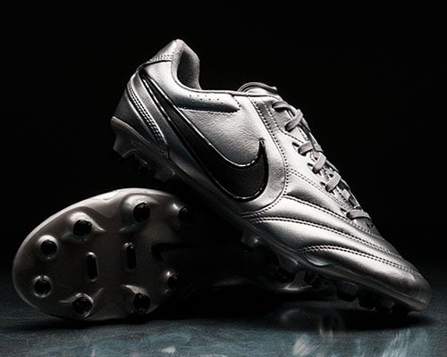 Pair of silver special edition Ligeras arranged: one sideways showing the sole plate. Other boot in front ramped on and showing outside profile with classic stitching and Nike Swoosh.