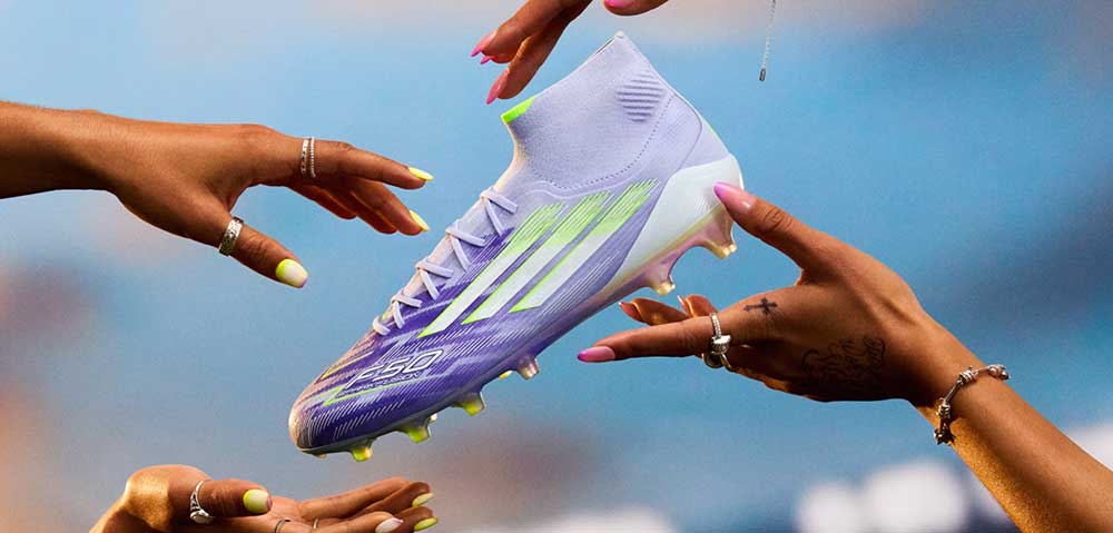 adidas F50 Sparkfusion Damen-Topmodell mit mittelhohem Kragen schwebend in der Mitte, rundherum Damenhände mit lackierten Fingernägeln, die nach dem neuen Speed-Fußballschuh für Damen greifen wollen