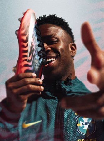 Vini Jr. in Brasil training gear holding a Nike Mercurial Vapor 17 FG cleat in front of his face covering the right eyes
